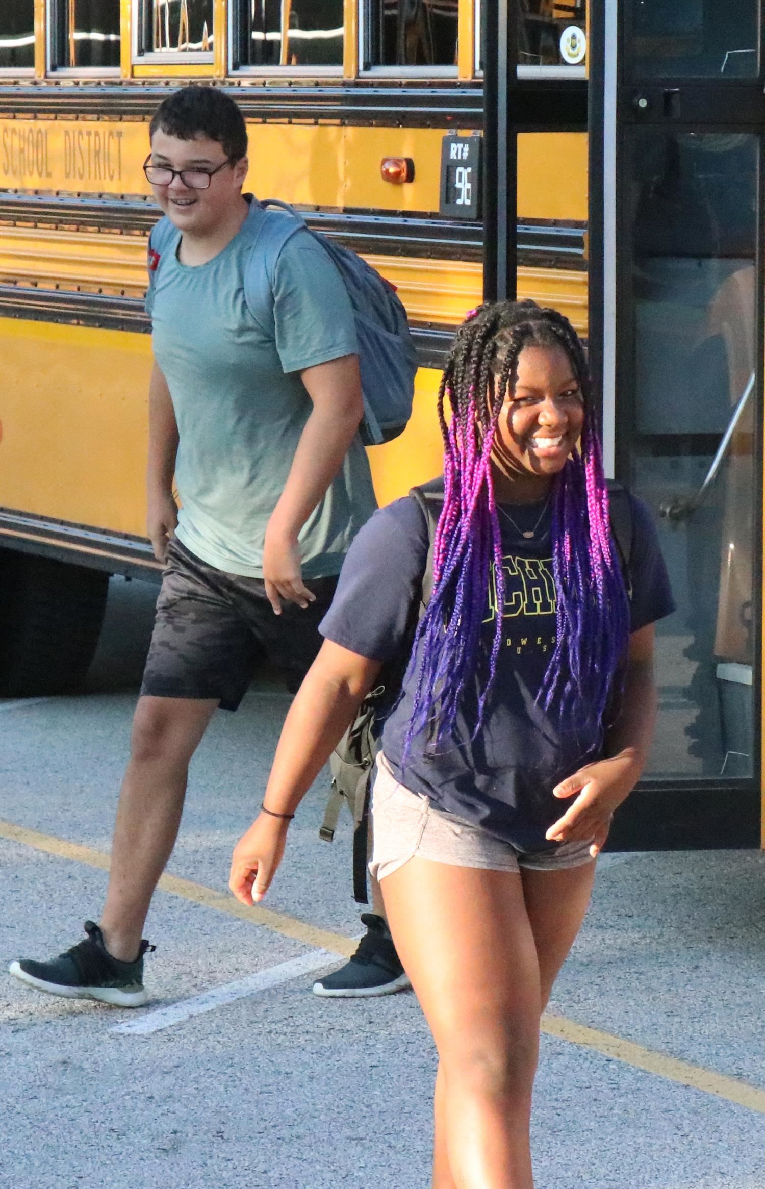 A student smiles on her way off the bus into her school building